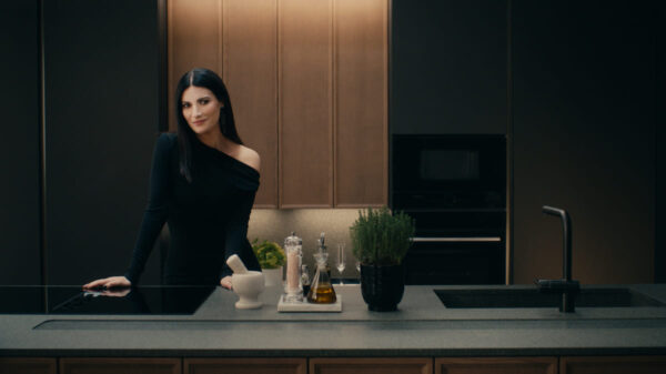 Laura Pausini nella cucina Poetica con ante telaio in Impiallacciato Frassino Cacao e ante Pet in Microdecor Space Black; a destra boiserie Vertical System. Sullo sfondo, la composizione con pensili Sail completa l’ambiente